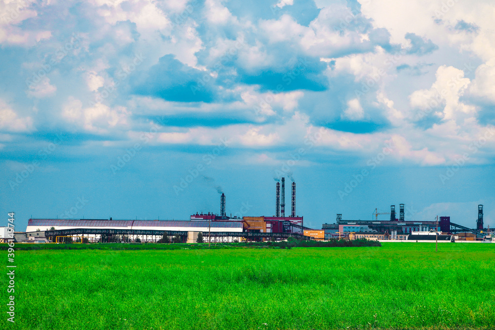 Fumes of a mining plant against the sky and green grass.