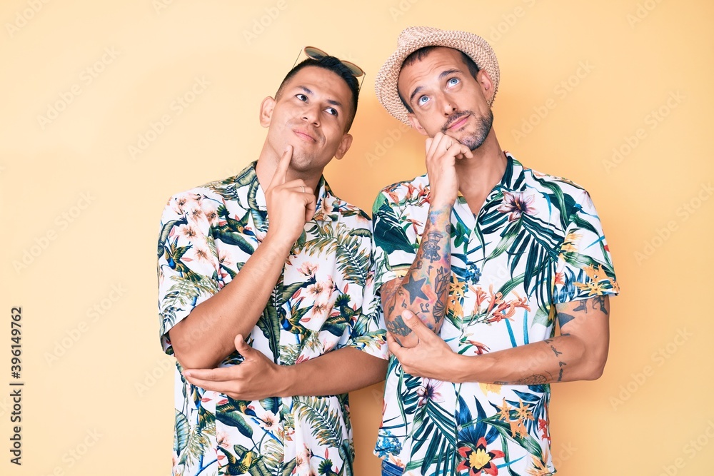 Young gay couple of two men wearing summer hat and hawaiian shirt with hand on chin thinking about question, pensive expression. smiling and thoughtful face. doubt concept. Young gay couple of two men wearing summer hat and hawaiian shirt with hand on chin thinking about question, pensive expression. smiling and thoughtful face. doubt concept.