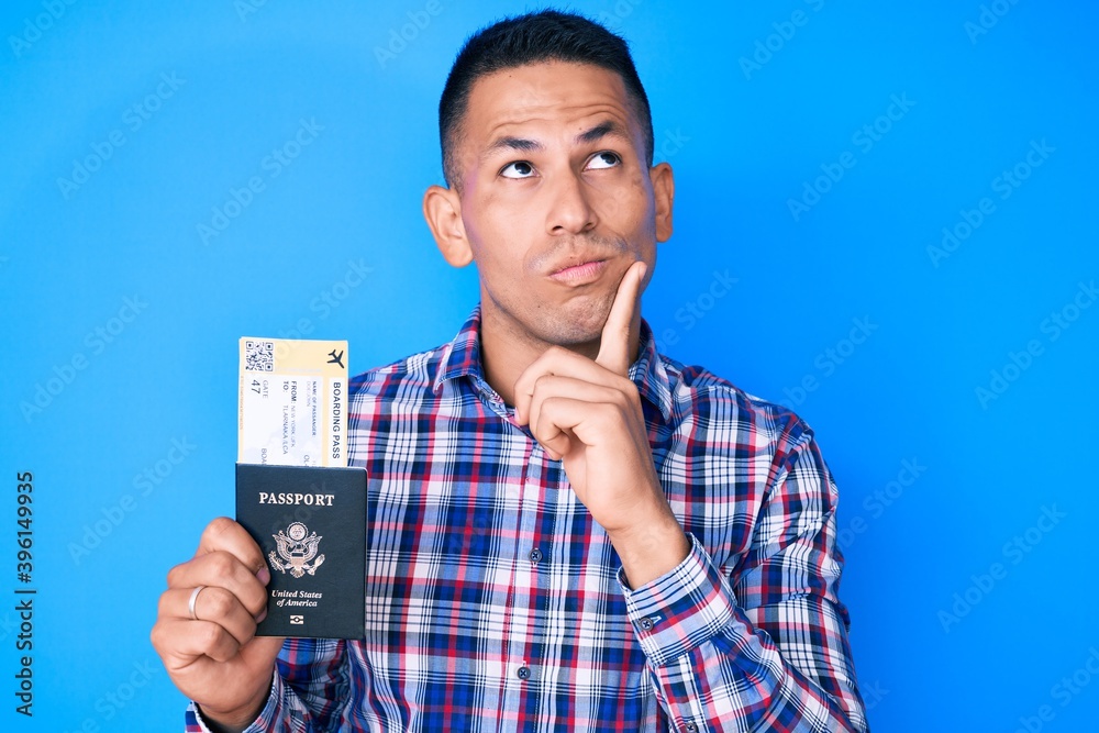 Young handsome latin man holding united states passport and boarding pass serious face thinking about question with hand on chin, thoughtful about confusing idea Young handsome latin man holding united states passport and boarding pass serious face thinking about question with hand on chin, thoughtful about confusing idea