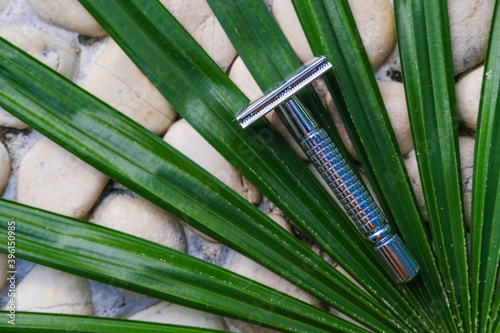 Reusable steel double edged eco-friendly safety razor on stone background with tropical palm leaf. Zero waste sustainable plastic free lifestyle