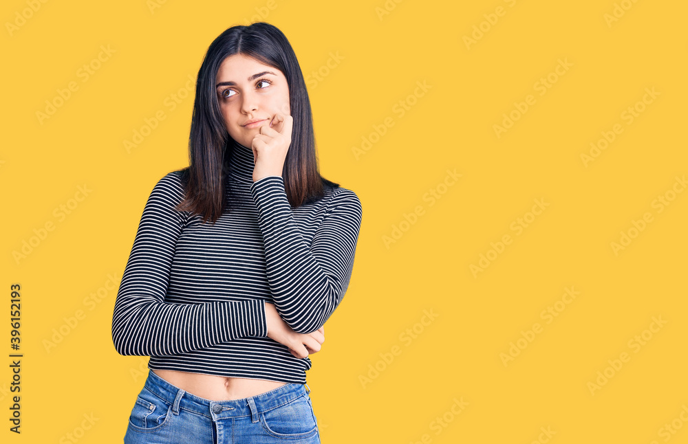 Young beautiful girl wearing striped t shirt serious face thinking about question with hand on chin, thoughtful about confusing idea Young beautiful girl wearing striped t shirt serious face thinking about question with hand on chin, thoughtful about confusing idea