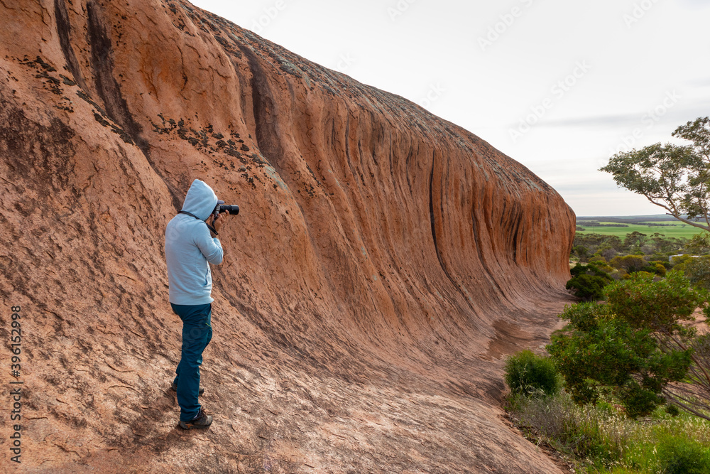 Male tourist taking pictures of Pildappa rock, wave rock in Australia rich in pink granites. Camping place and picnic area by the rock. Eyre Peninsula, Gawler ranges, South Australia's granite country