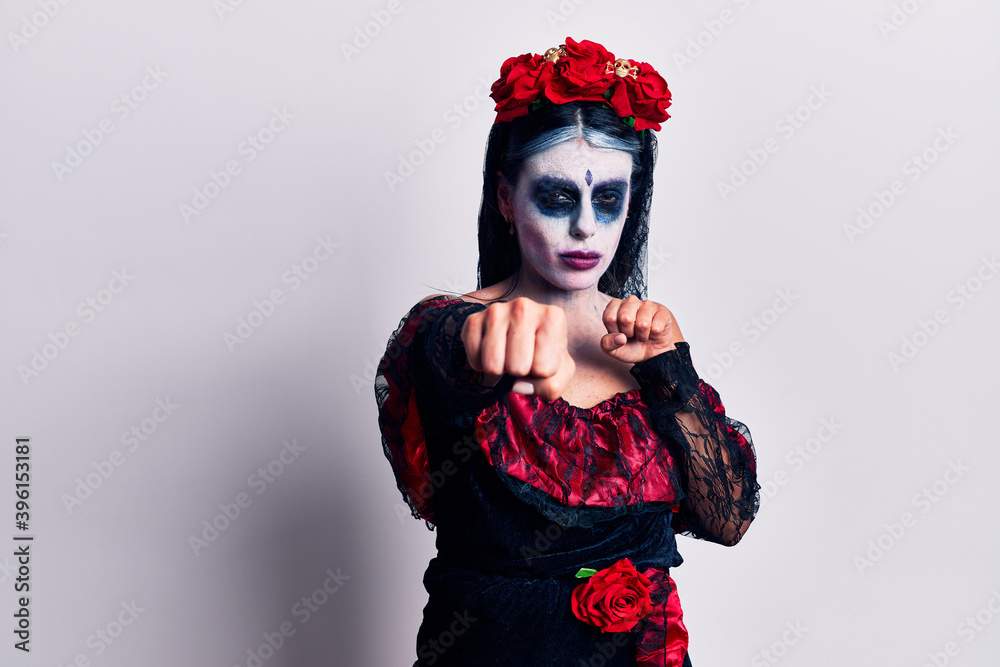 Young woman wearing mexican day of the dead makeup punching fist to fight, aggressive and angry attack, threat and violence