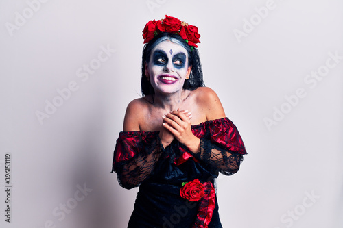 Young woman wearing mexican day of the dead makeup laughing nervous and excited with hands on chin looking to the side © Krakenimages.com