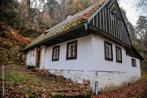 Small old white wooden house near village Mala Skala, moss roof, traditional hut or cottage surrounded by trees in autumn forest, Bohemian Paradise, Czech Republic