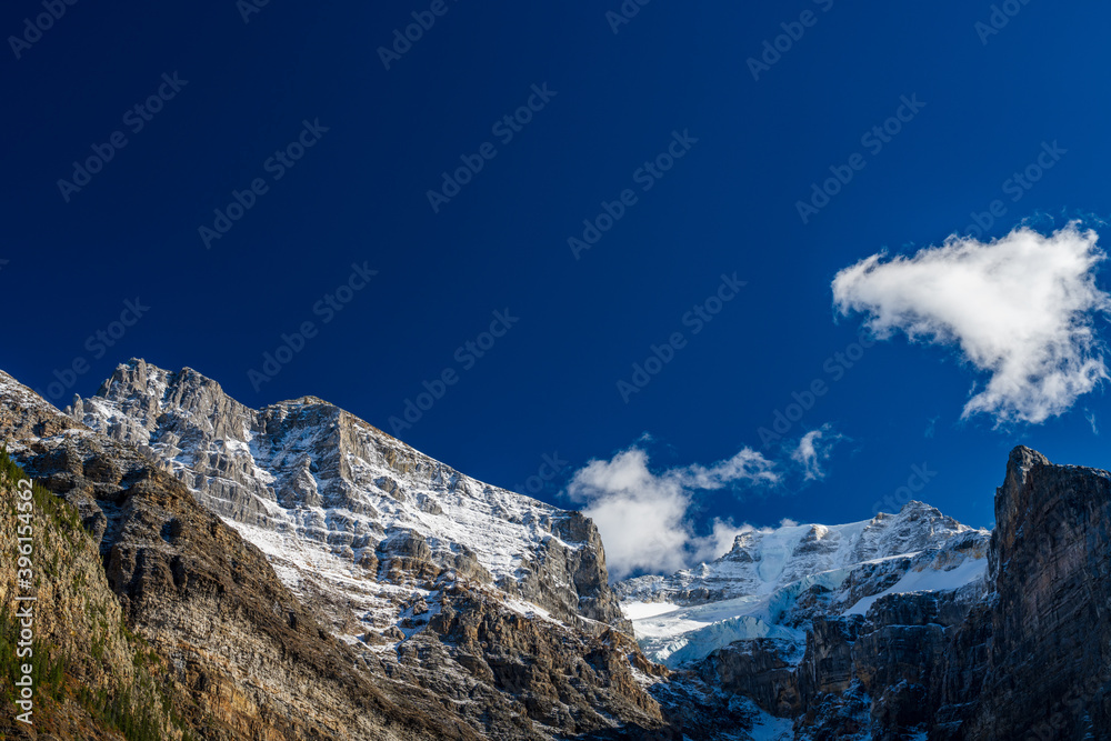 Snow-covered majestic mountain peaks with dark blue sky and flowing clouds in the background. Valley of the Ten Peaks, Moraine lake. Banff National Park, Canadian Rockies, Alberta, Canada.