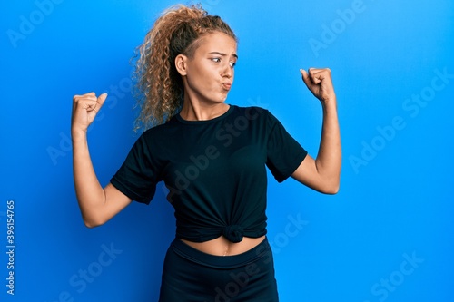 Beautiful caucasian teenager girl wearing black sportswear showing arms muscles smiling proud. fitness concept.