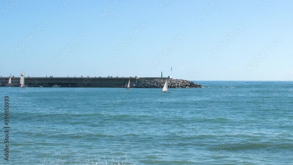 Sailing boats sailing near the harbor and people strolling away on the jetty. Sailing boats sailing near the harbor and people strolling away on the jetty.