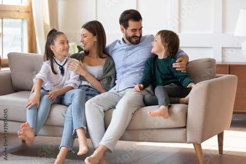 Overjoyed young parents with two little kids sit rest on comfortable couch in new home. Smiling Caucasian family renters relax in living room in own modern design house. Relocation, rental concept. © fizkes