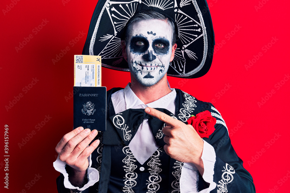Young man wearing mexican day of the dead costume holding united states passport and boarding pass smiling happy pointing with hand and finger