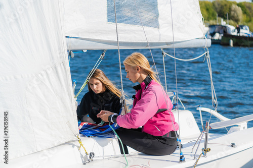 Before the competition on sailing boats two cute girls athletes equip their sailing yacht.