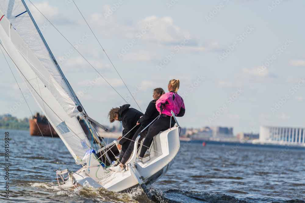 Naklejka premium A beautiful picture with a sports yacht on the background of an urban landscape floating under full sails on a wide river