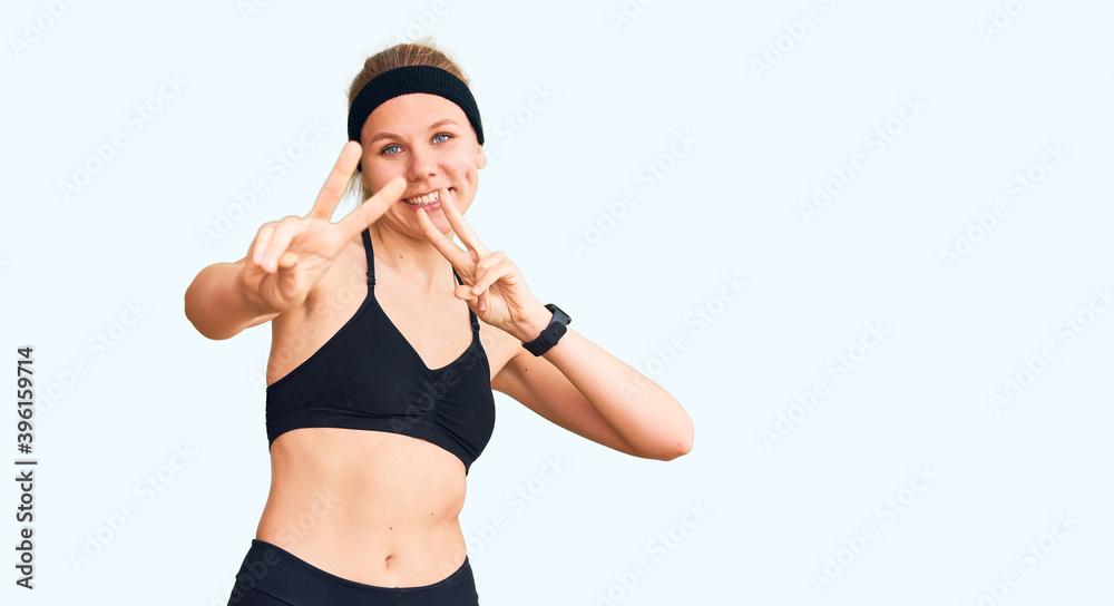 Young beautiful blonde woman wearing sportswear smiling looking to the camera showing fingers doing victory sign. number two. Young beautiful blonde woman wearing sportswear smiling looking to the camera showing fingers doing victory sign. number two.