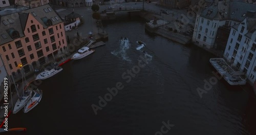 Beautiful aerial drone footage that follows kids who are riding jet skis in Brosundet canal in Alesund, the most beautiful town in Norway at dusk. photo