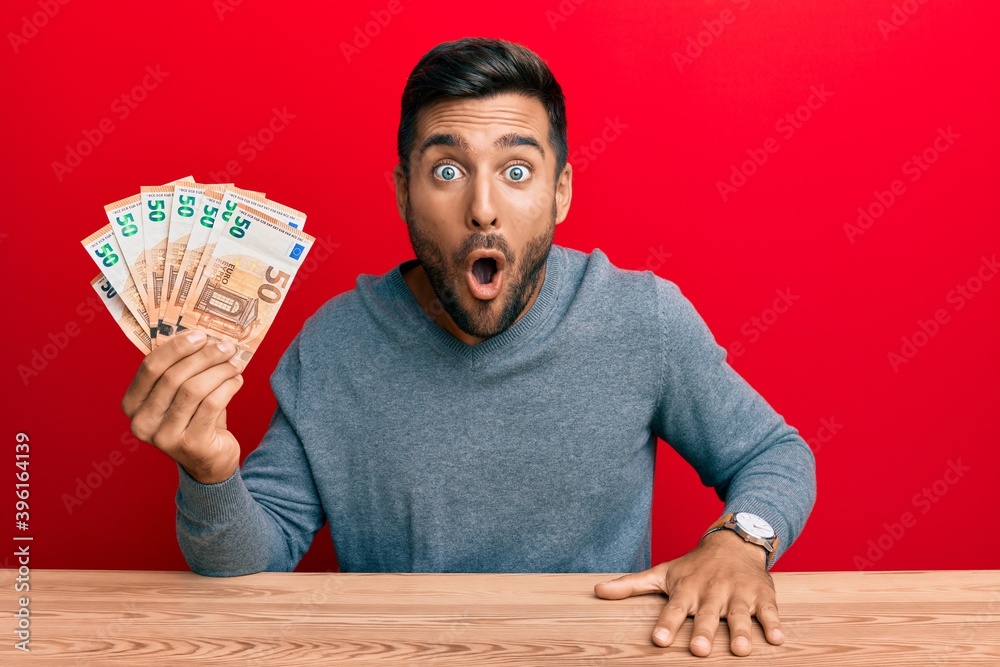Handsome hispanic man holding bunch of 50 euro banknotes scared and amazed with open mouth for surprise, disbelief face Handsome hispanic man holding bunch of 50 euro banknotes scared and amazed with open mouth for surprise, disbelief face