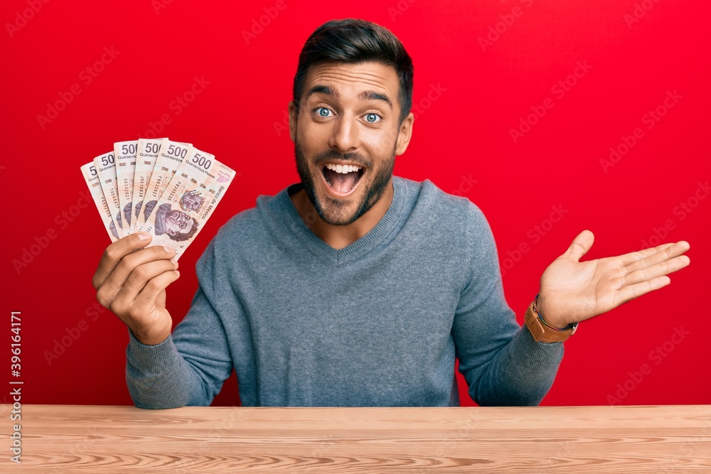 Handsome hispanic man holding mexican pesos celebrating achievement with happy smile and winner expression with raised hand Handsome hispanic man holding mexican pesos celebrating achievement with happy smile and winner expression with raised hand