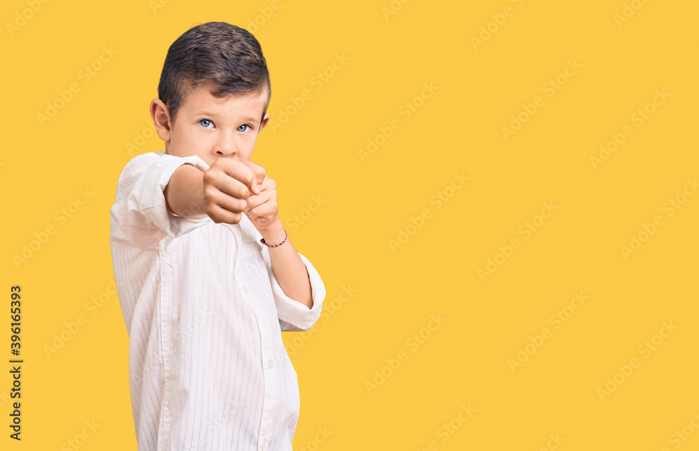 Cute blond kid wearing elegant shirt punching fist to fight, aggressive and angry attack, threat and violence Cute blond kid wearing elegant shirt punching fist to fight, aggressive and angry attack, threat and violence
