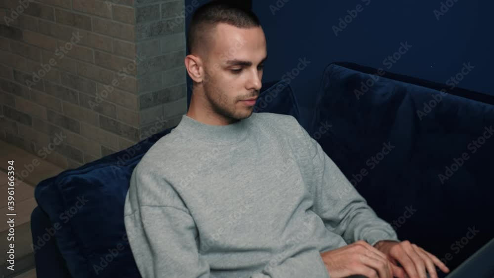 Relaxed serious man student freelancer using laptop device leaning on sofa at home office, focused working distantly typing on notebook in apartment Relaxed serious man student freelancer using laptop device leaning on sofa at home office, focused working distantly typing on notebook in apartment