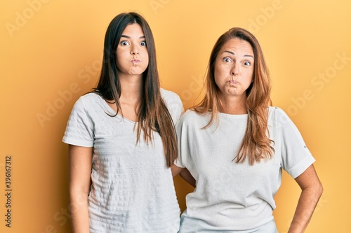 Hispanic family of mother and daughter wearing casual white tshirt puffing cheeks with funny face. mouth inflated with air  crazy expression.