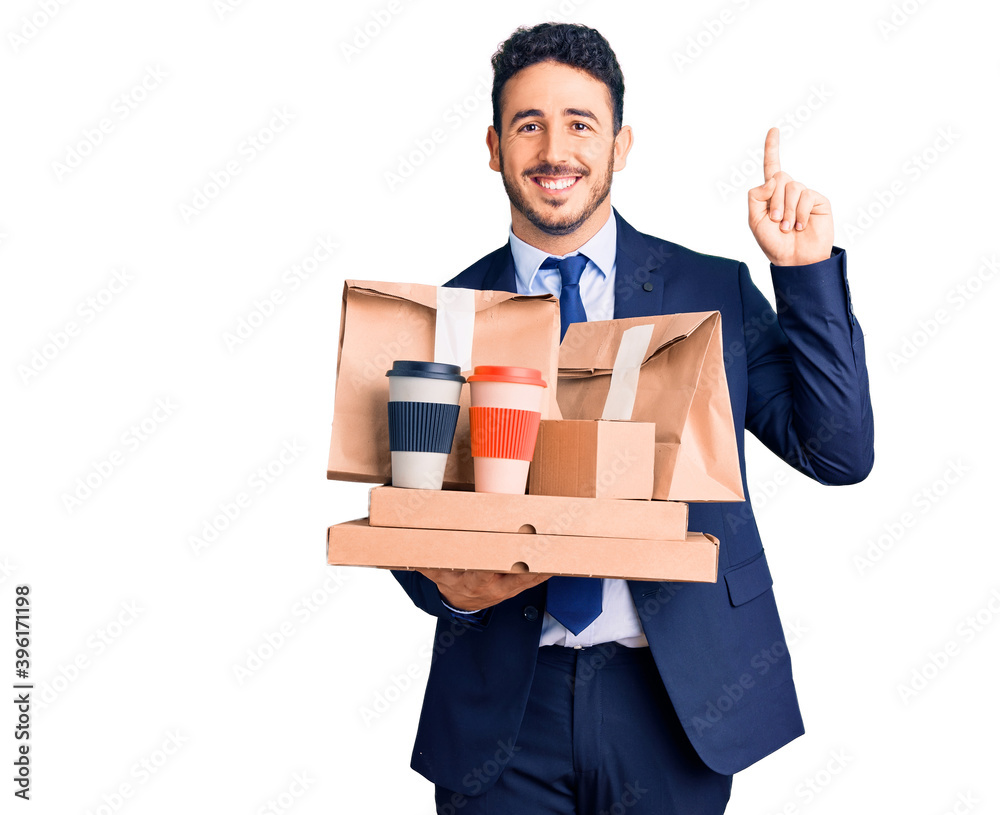 Young hispanic man wearing suit holding takeaway coffee and food surprised with an idea or question pointing finger with happy face, number one Young hispanic man wearing suit holding takeaway coffee and food surprised with an idea or question pointing finger with happy face, number one