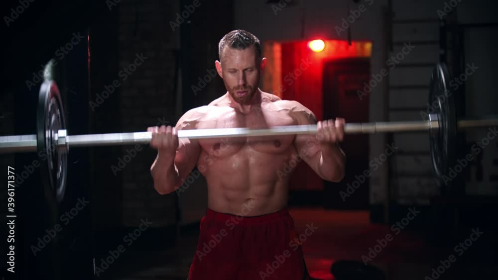 Tough man covered in sweat doing exercises - pulling up a heavy bar with an effort Tough man covered in sweat doing exercises - pulling up a heavy bar with an effort