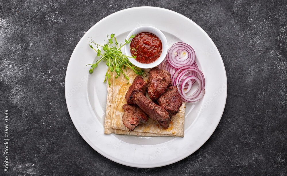 shashlik, with sauce, onions, and lavash, on a white plate, on a dark background shashlik, with sauce, onions, and lavash, on a white plate, on a dark background