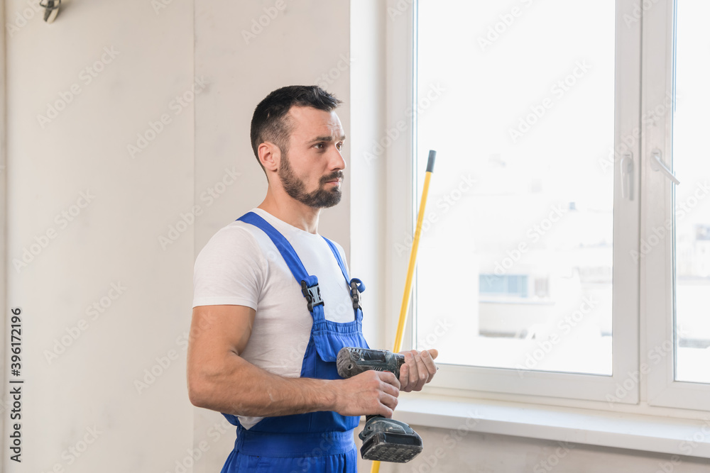 A builder in a blue overalls holds a tape measure in his hand A builder in a blue overalls holds a tape measure in his hand