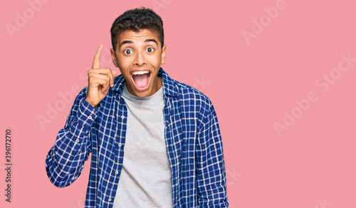 Young handsome african american man wearing casual clothes pointing finger up with successful idea. exited and happy. number one.