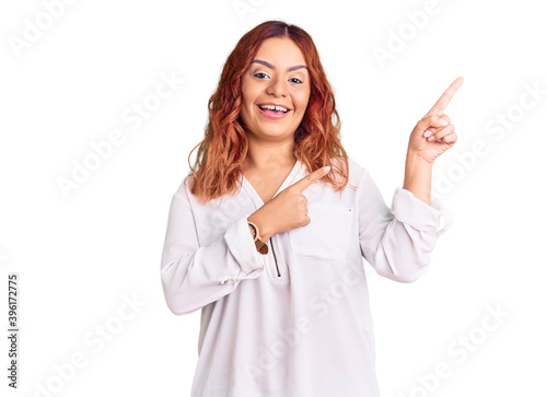 Young latin woman wearing casual clothes smiling and looking at the camera pointing with two hands and fingers to the side.