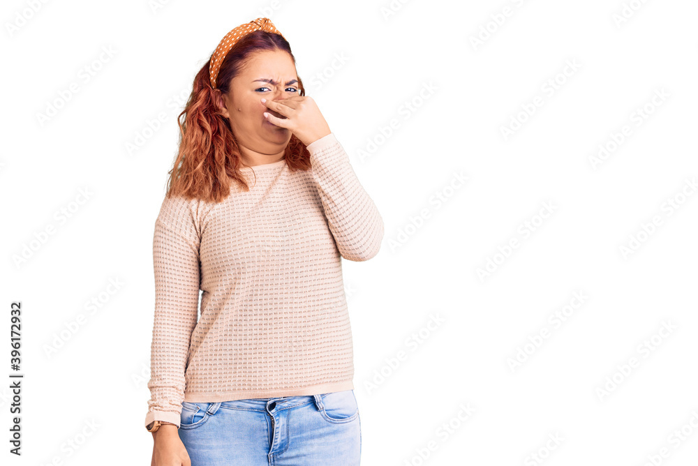 Young latin woman wearing casual clothes and diadem smelling something stinky and disgusting, intolerable smell, holding breath with fingers on nose. bad smell Young latin woman wearing casual clothes and diadem smelling something stinky and disgusting, intolerable smell, holding breath with fingers on nose. bad smell