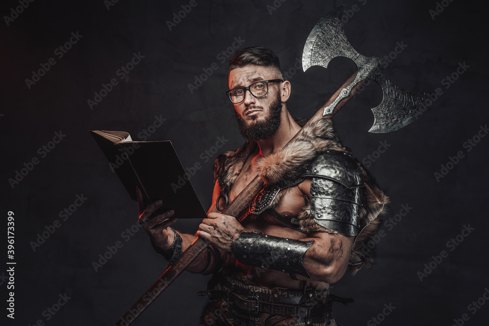 Holding two handed axe on his shoulder nordic fighter weared with glasses poses in dark background with book.