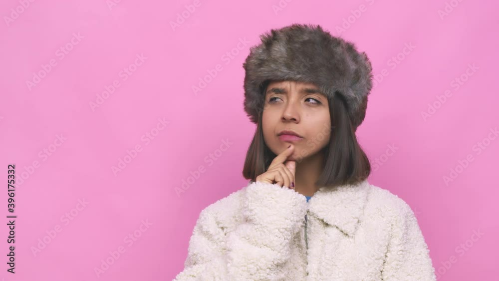 Young hispanic woman wearing a winter hat face closeup looking sideways with doubtful and skeptical expression Young hispanic woman wearing a winter hat face closeup looking sideways with doubtful and skeptical expression