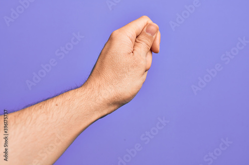 Hand of caucasian young man showing fingers over isolated purple background holding blank space with thumb finger, business and advertising