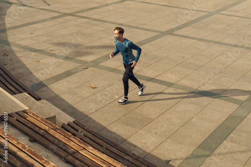 Athletic and handsome young male wearing a gray mask. Young athlete wearing a mask to train outside. Fit muscular athlete dressed in sportswear wearing a mask while jogging.