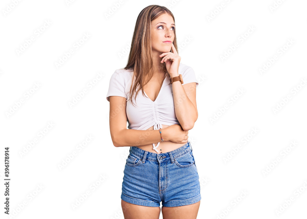 Young beautiful blonde woman wearing casual white tshirt with hand on chin thinking about question, pensive expression. smiling with thoughtful face. doubt concept. Young beautiful blonde woman wearing casual white tshirt with hand on chin thinking about question, pensive expression. smiling with thoughtful face. doubt concept.