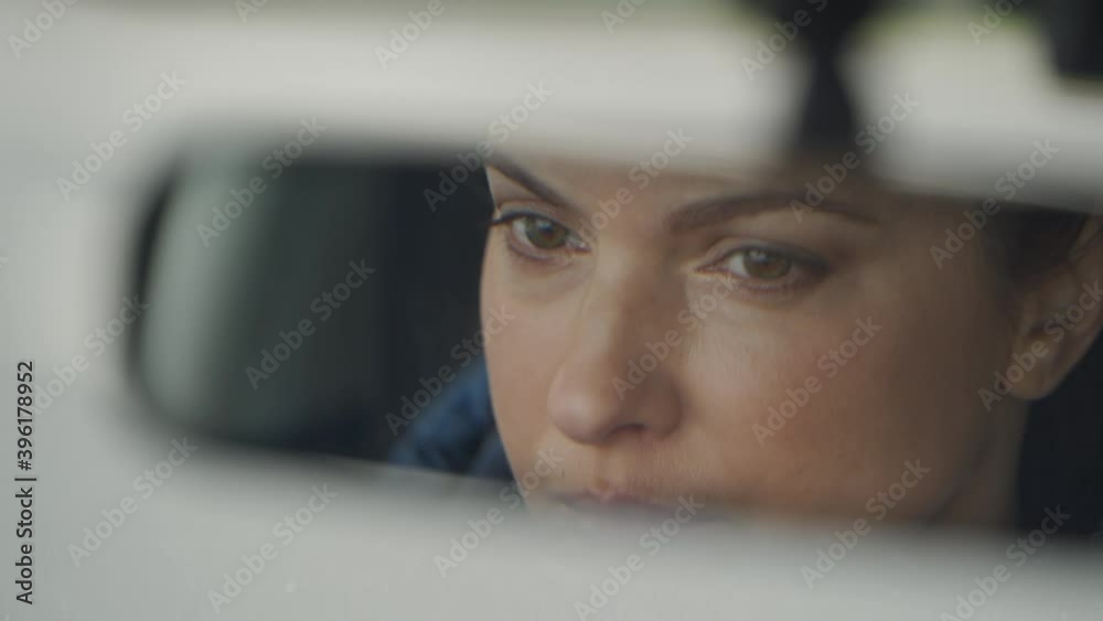 Brunette woman sitting behind the wheel driving car female driver face in rear view mirror closeup.