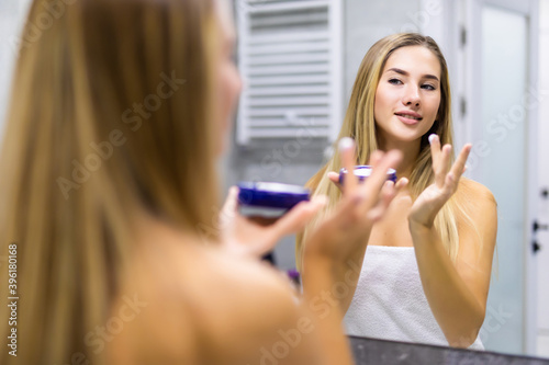 Happy young woman applying cream in bathroom at home