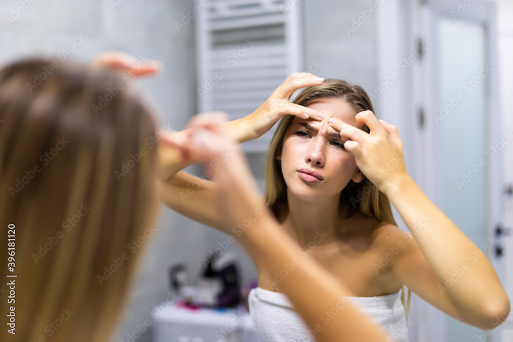 Fototapeta premium Portrait of beautiful young woman squeezing pimples while looking at the mirror