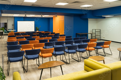 Conference hall with orange and blue chairs and blank screen