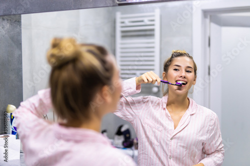 Beautiful young woman brushing teeth in front of her bathroom mirror.