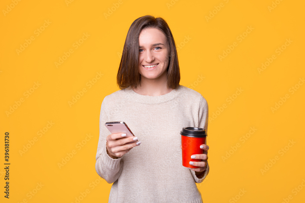Happy young woman standing smile, holding mobile phone and coffee paper cup and looking at camera