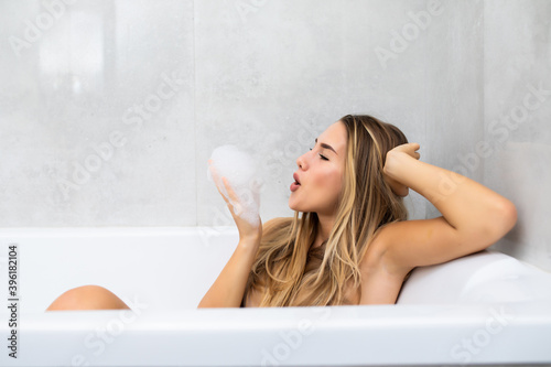 Happy young woman in bathtub playing with foam