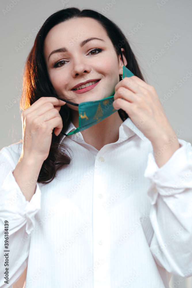 Caucasian girl with a beautiful smile wearing a white shirt is taking off / putting on a disposable Christmas designed face mask Caucasian girl with a beautiful smile wearing a white shirt is taking off / putting on a disposable Christmas designed face mask