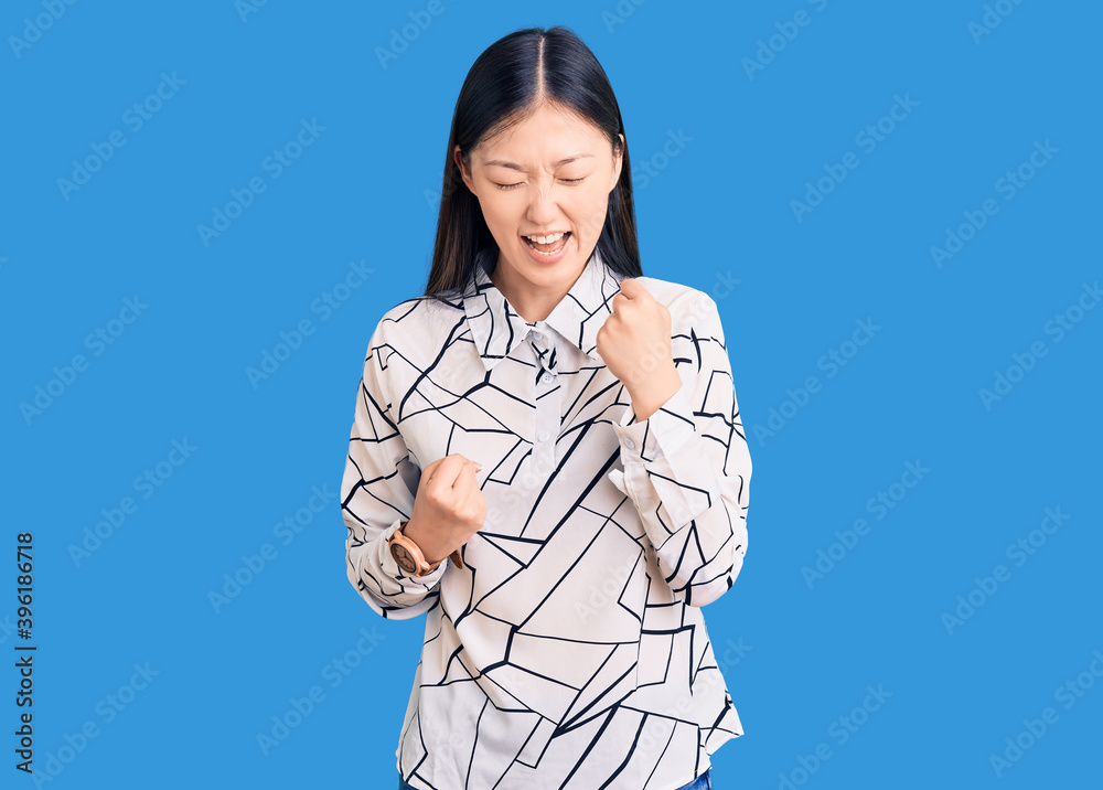 Young beautiful chinese woman wearing casual shirt celebrating surprised and amazed for success with arms raised and eyes closed. winner concept. Young beautiful chinese woman wearing casual shirt celebrating surprised and amazed for success with arms raised and eyes closed. winner concept.