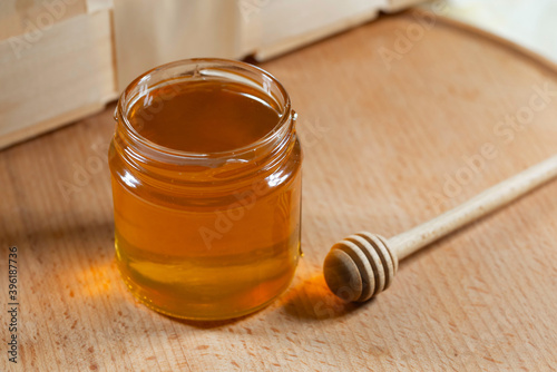 Honey in a glass jar with a wooden honey dipper on a wooden table. Healthy organic honey