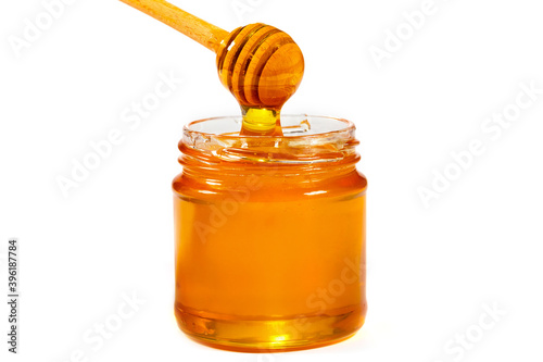 Glass jar of honey with a wooden ladle isolated on white. Organic honey, healthy food, close-up