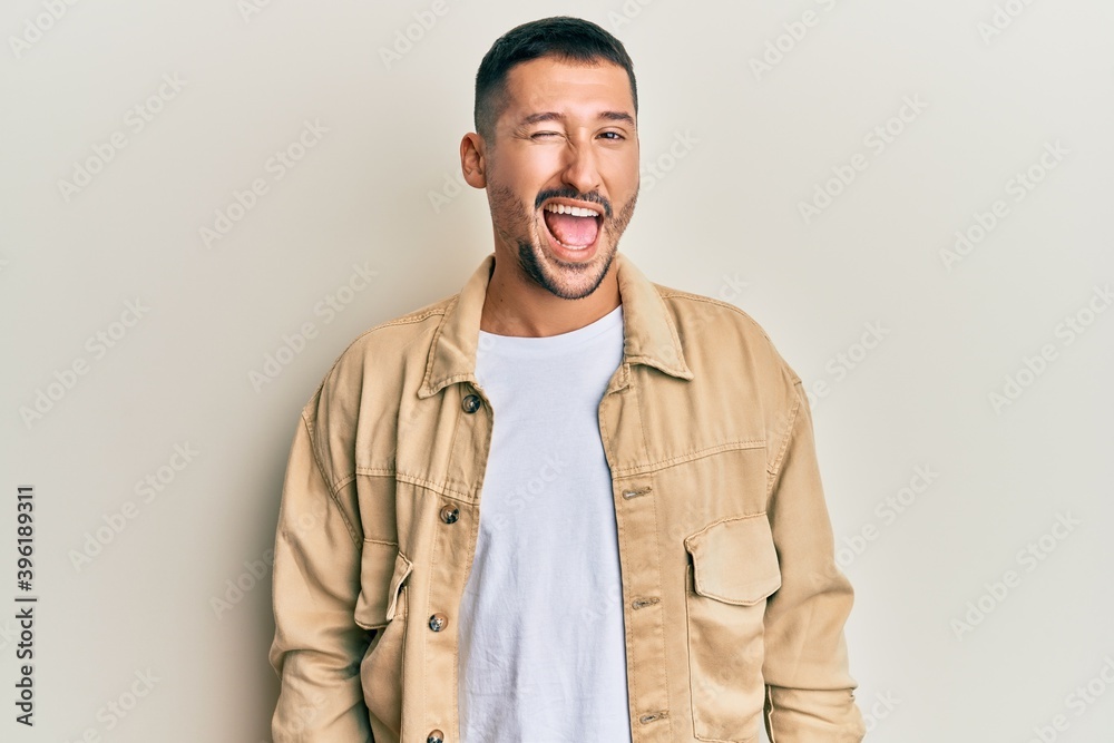 Fototapeta premium Handsome man with tattoos wearing casual brown denim jacket winking looking at the camera with sexy expression, cheerful and happy face.