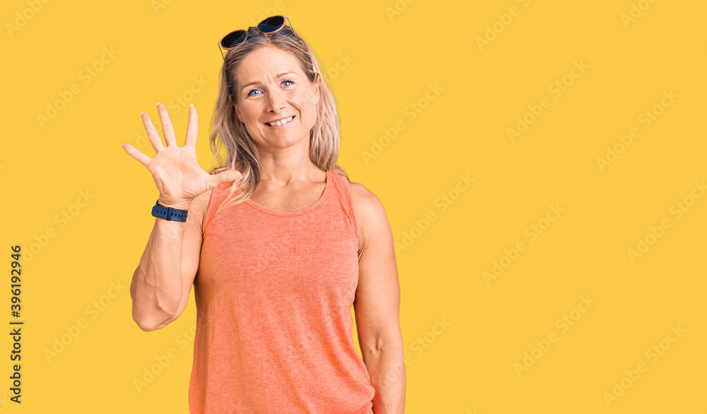 Middle age fit blonde woman wearing casual summer clothes and sunglasses showing and pointing up with fingers number five while smiling confident and happy. Middle age fit blonde woman wearing casual summer clothes and sunglasses showing and pointing up with fingers number five while smiling confident and happy.