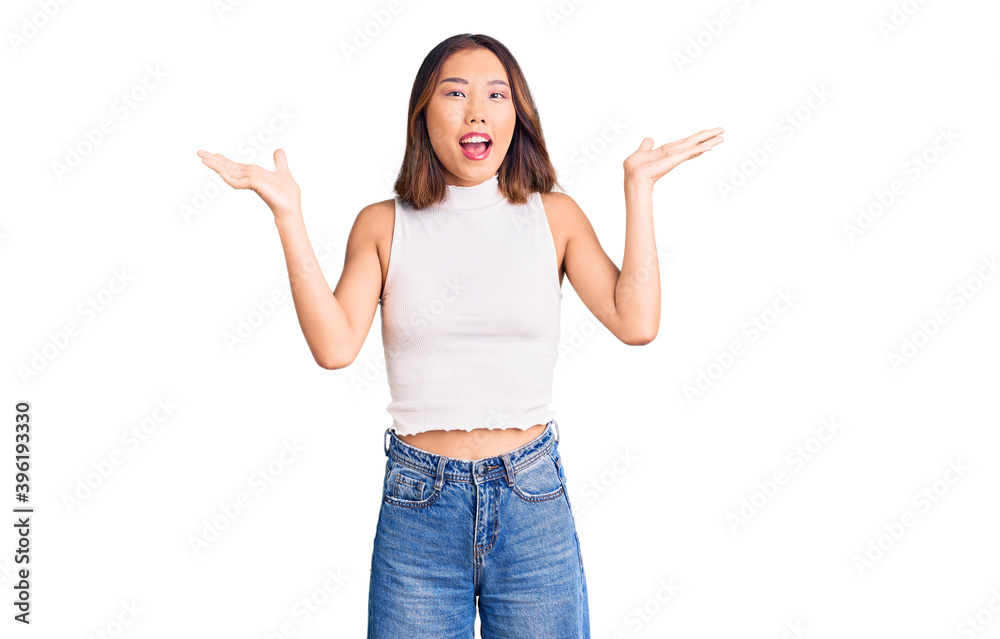Young beautiful chinese girl wearing casual clothes celebrating victory with happy smile and winner expression with raised hands Young beautiful chinese girl wearing casual clothes celebrating victory with happy smile and winner expression with raised hands