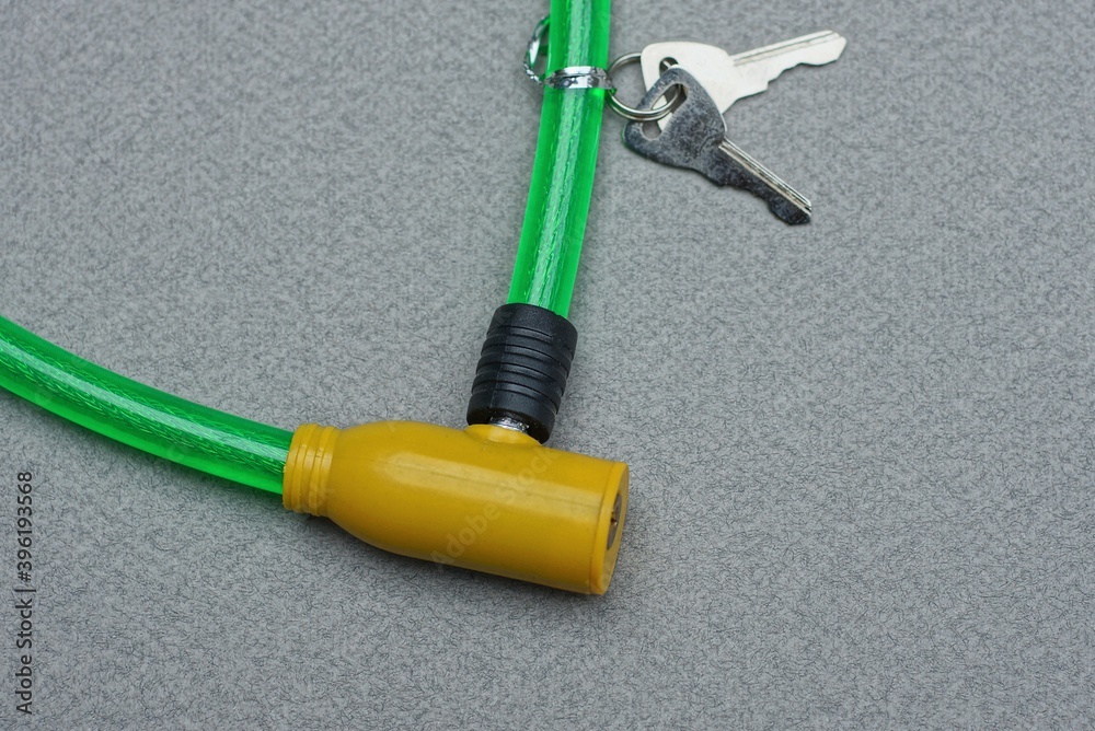part on a bicycle lock with a yellow metal core and a green plastic cable and two keys lies on a gray table